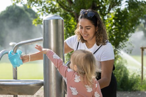 Fachfrau Betreuung bei der Arbeit mit einem Kind vor einem Brunnen. 