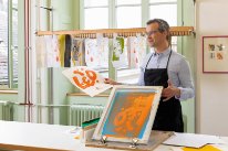 Ein Mitarbeitender des Kantons Basel-Stadt beim Siebdruck mit oranger Farbe. 
